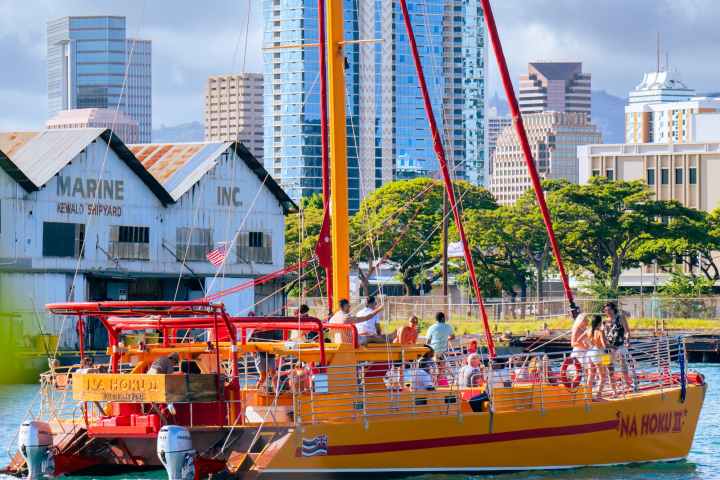 Yellow sailboat on water near city buildings and trees.