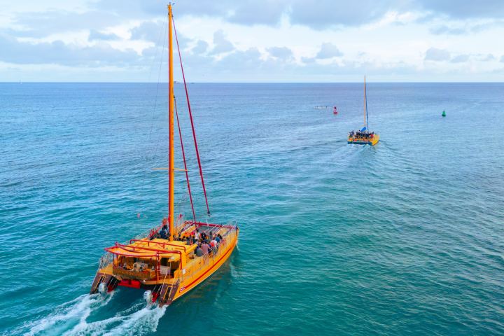 Two yellow sailboats with orange sails on blue ocean under cloudy sky, sailing away.